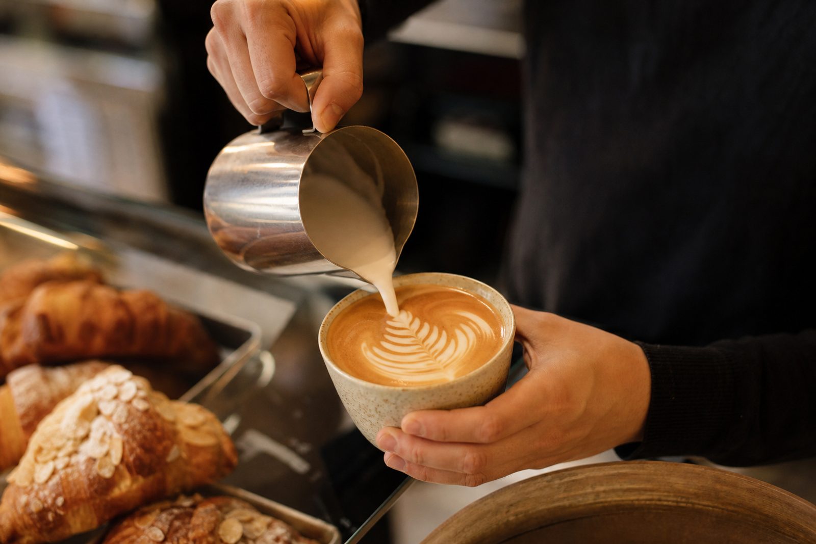 A barista pouring milk into a latte